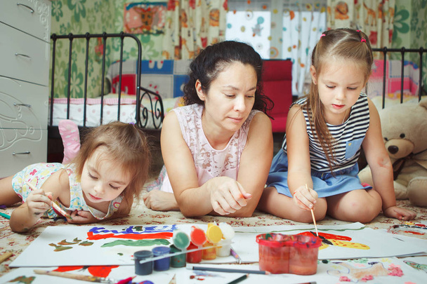 Мама и дочери рисуют картины и лежат на полу
 - Фото, изображение
