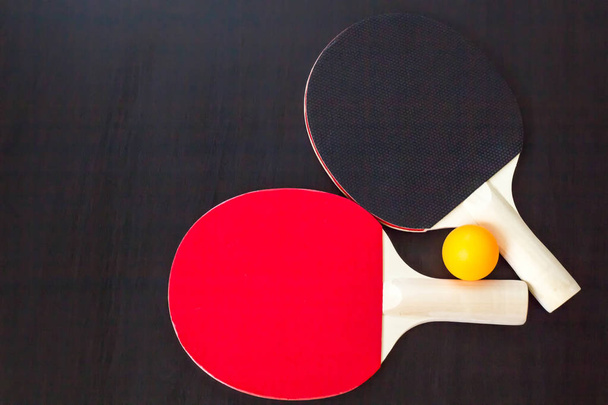 Duas raquetes de tênis de mesa ou ping pong e bola em um fundo preto
 - Foto, Imagem