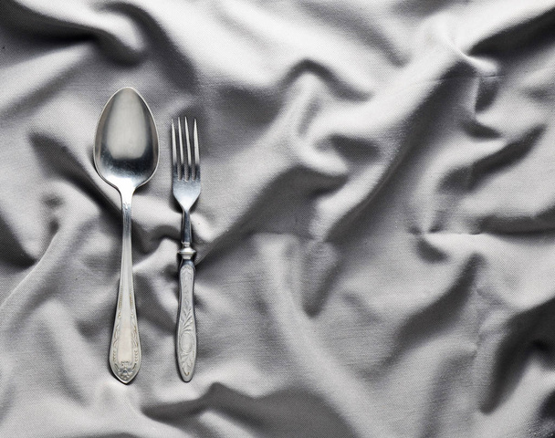 Lepel en vork op een grijze zijden tafellaken. Vintage bestek. Kopieer ruimte. Bovenaanzicht. - Foto, afbeelding