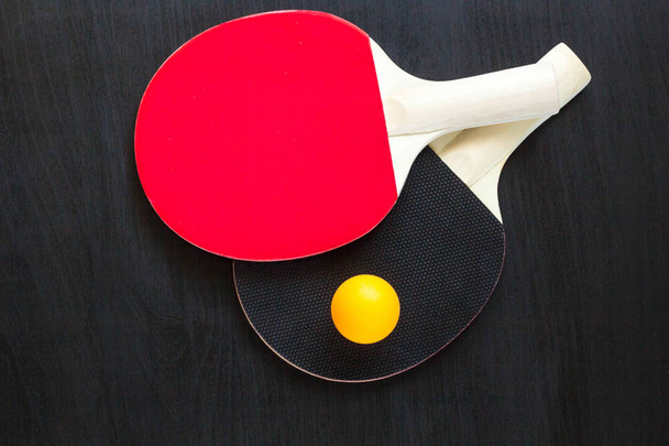 Dos raquetas de tenis de mesa o ping pong y pelota sobre fondo negro
 - Foto, Imagen