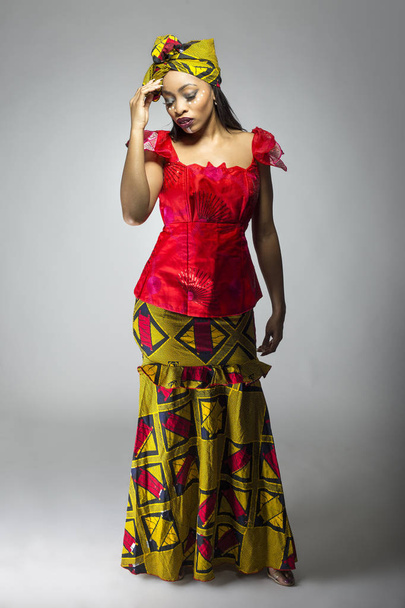 Black female showing african pride by wearing a traditional Nigerian dress and head scarf with tribal face markings or cosmetic makeup.  The costume is red and yellow and shows cultural fashion. - Фото, изображение
