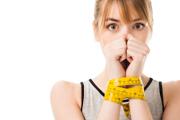 scared young woman covering face with hands tied in measuring tape isolated on white - Photo, image
