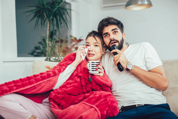 Beautiful young couple watching TV in living room. - 写真・画像