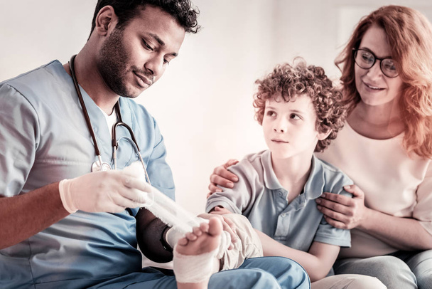 Serious doctor applying bandage on teen foot - Foto, imagen