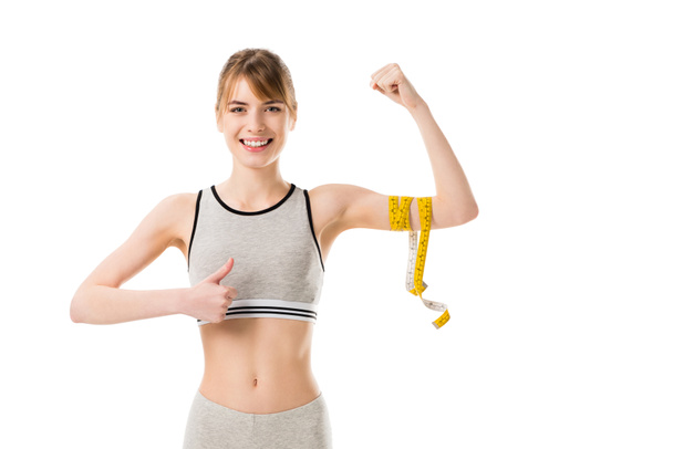 joven mujer delgada mostrando sus bíceps atados con cinta métrica y el pulgar hacia arriba aislado en blanco
 - Foto, imagen