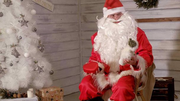 Weihnachtsmann sitzt in einem Stuhl und versucht, ein Spielzeug als Geschenk zu stopfen - Foto, Bild