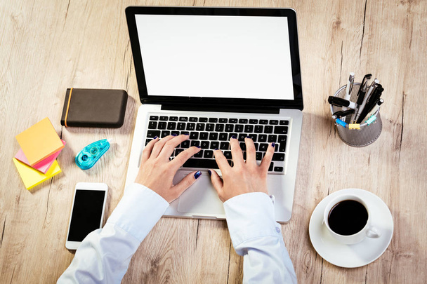 Widok z góry samicy ręce pracy na laptopie. Smartphone, akcesoria biurowe różnych i filiżankę kawy jest na stole.  - Zdjęcie, obraz