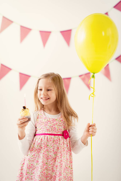 Hermosa niña alegre sosteniendo globo y pequeño pastel de cumpleaños con vela
. - Foto, Imagen