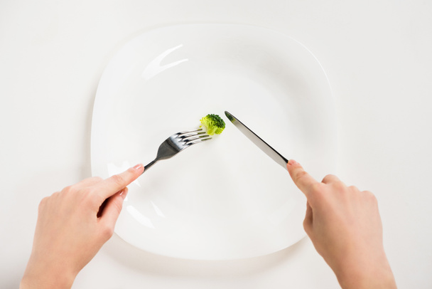 abgeschnittene Aufnahme einer Frau, die mit Gabel und Messer ein kleines Stück Brokkoli isst - Foto, Bild