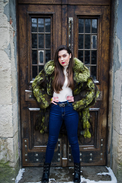 Brunette girl in green fur coat against old wooden doors. - 写真・画像