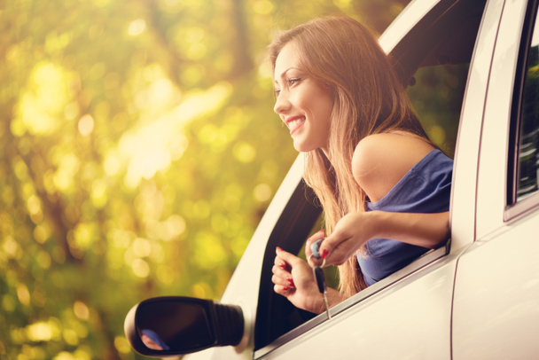 Mladá krásná žena sedí v autě, v lese a hledá další směr. Ona drží klíče od auta a koukal. - Fotografie, Obrázek