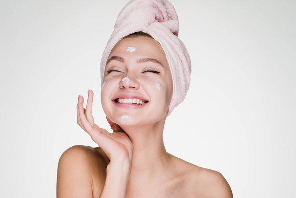 happy woman with a towel on her head apply cream on her face - Foto, Bild