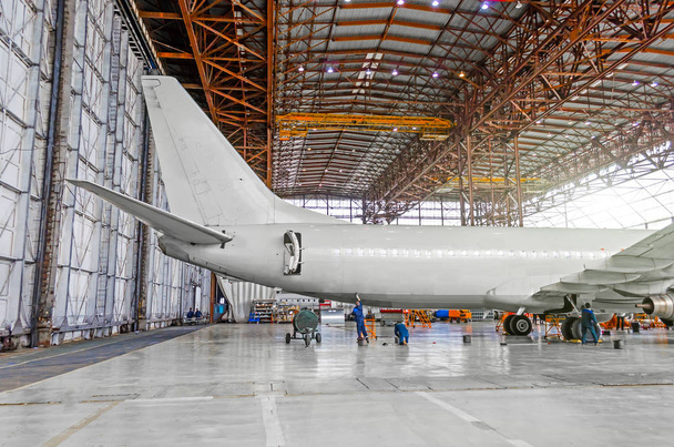 Aviones de pasajeros en mantenimiento de reparación, una vista de la cola y la parte trasera del fuselaje en el hangar del aeropuerto
. - Foto, imagen