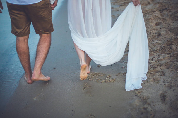 Young man and woman holding hands and walking on river beach - 写真・画像