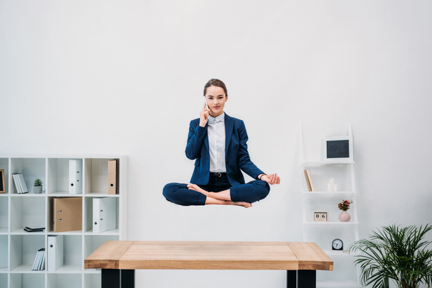businesswoman talking by smartphone and looking at camera while levitating in office - Valokuva, kuva