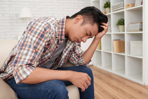 unavený Asiat s bolestí hlavy, sedí na gauči doma - Fotografie, Obrázek