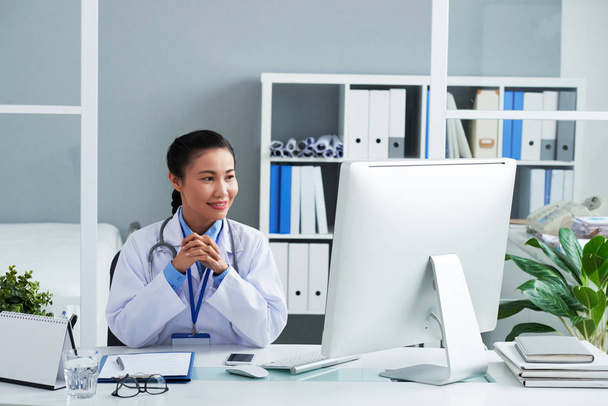 女性のアジア医師オフィスに座って彼女のタブレットとコンピューターの画面上の情報の読み取り - 写真・画像