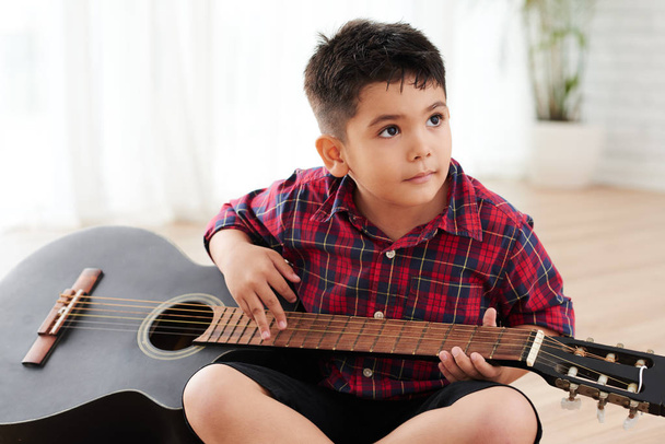 Smíšené rasy chlapec sedí na podlaze a hraje na kytaru - Fotografie, Obrázek