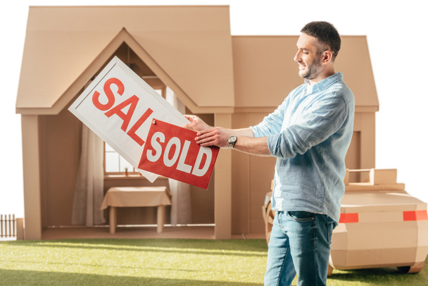 man holding sale and sold signboards in front of cardboard house isolated on white - Photo, Image