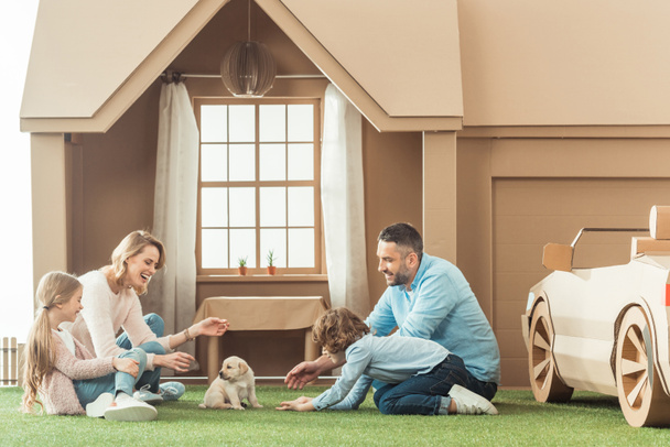 beautiful family with adorable puppy on yard of cardboard house - Photo, Image