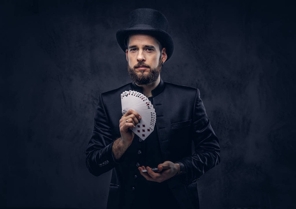 Чарівник, що показує трюк з граючими картками на темному тлі
. - Фото, зображення