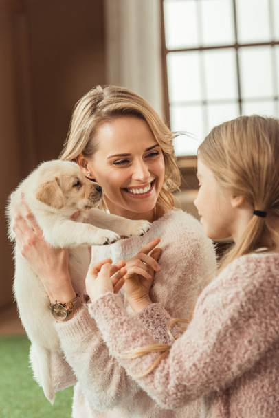beautiful mother and daughter playing with adorable labrador puppy - Foto, imagen