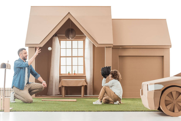 father teaching his son how to play baseball on yard of cardboard house - Photo, Image