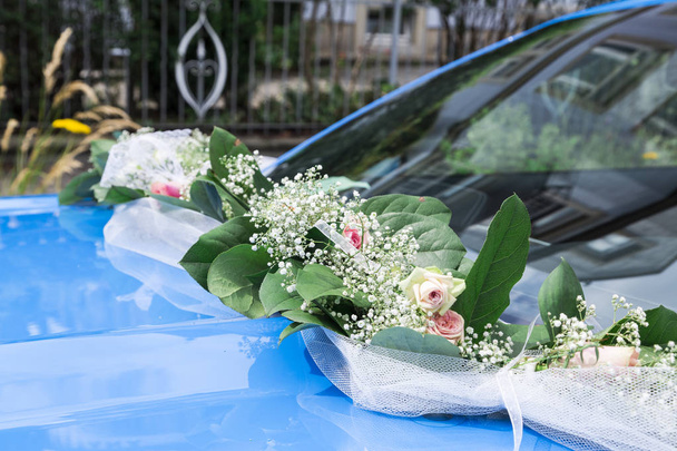 wedding wreath of fresh roses and silk ribbon on bumper of blue car - 写真・画像