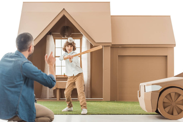 father teaching his son how to play baseball in front of cardboard house isolated on white - Photo, Image
