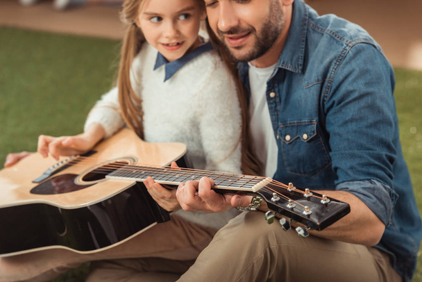 όμορφος πατέρας και η κόρη που παίζει κιθάρα, ενώ κάθεται στο γρασίδι - Φωτογραφία, εικόνα
