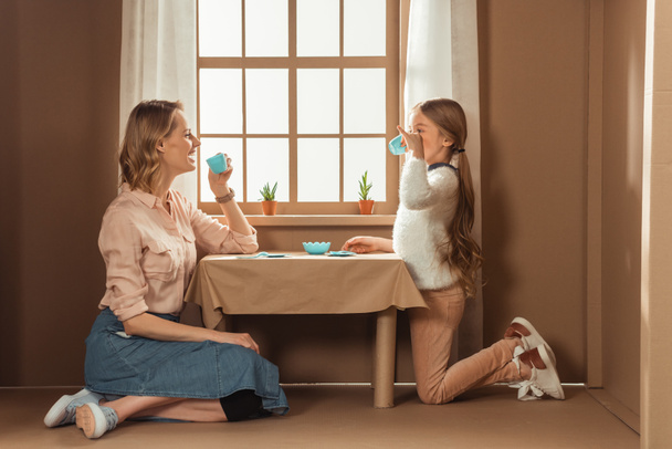 laughing mother and daughter having tea party in cardboard house - 写真・画像