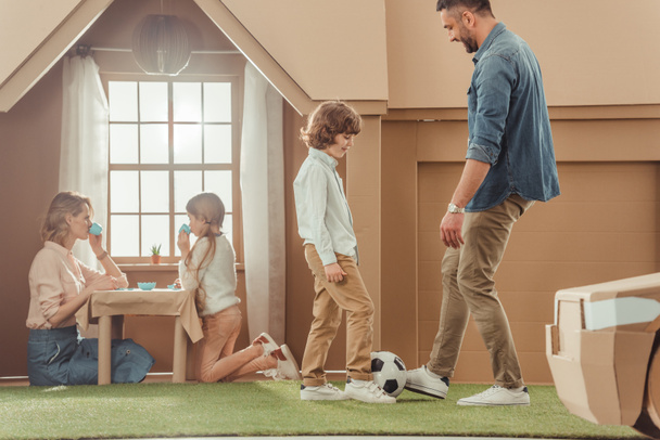 happy father teaching his som to play soccer on yard of cardboard house - Zdjęcie, obraz