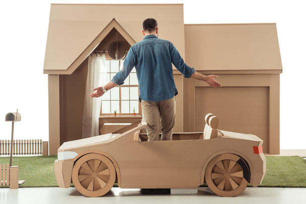rear view of man in cardboard car in front of cardboard house isolated on white - Photo, Image