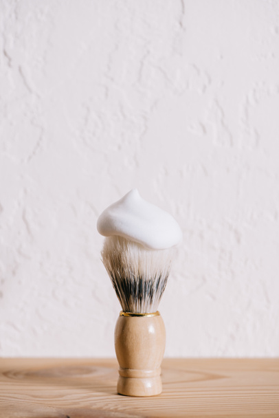 vista de cerca del cepillo de afeitar con espuma contra la pared blanca
 - Foto, imagen