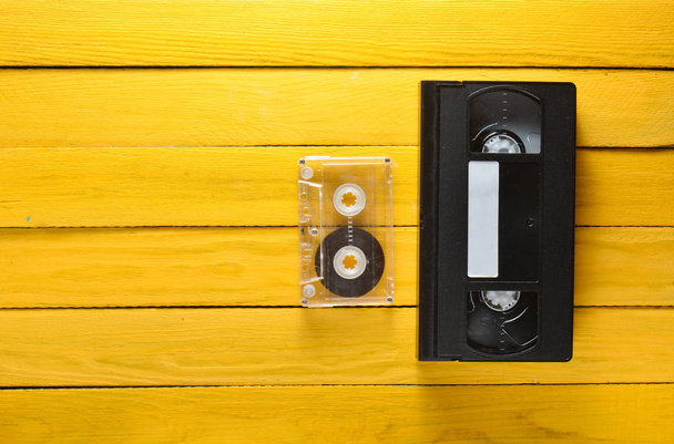 Vhs video cassette and audio cassette on a yellow wooden background. Retro media technology from the 80s. Top view. - Photo, Image