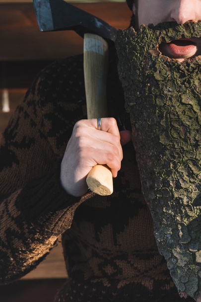 cropped shot of man with beard made of wood bark and axe in hand outdoors - Fotoğraf, Görsel