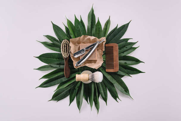 top view of arranged barber tools for shaving on green leaves isolated on grey - Foto, Bild