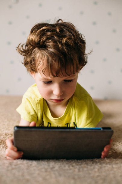 Cute little boy using a pad. Child playing with digital tablet lying on a bed. Free time. Tehnology and internet concept - Photo, image