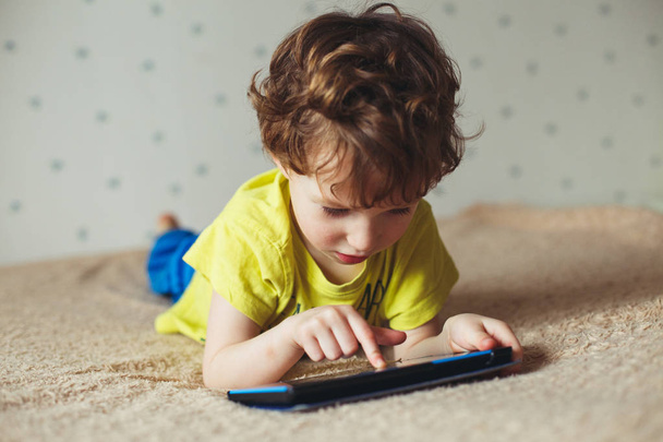 Little boy lying on bed and looking at tablet, using modern technology - Photo, image