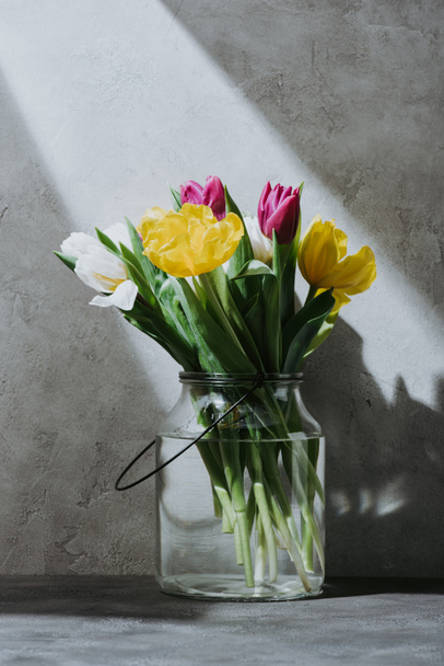 spring tulip flowers in glass jar on concrete surface with shadow - 写真・画像