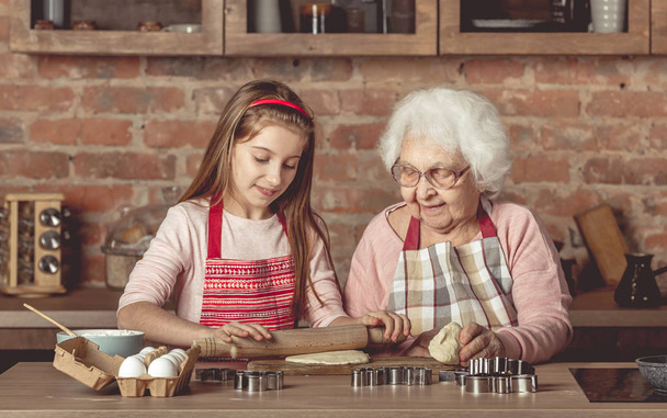 Elderly woman teaching a little girl to bake cookies - Photo, image