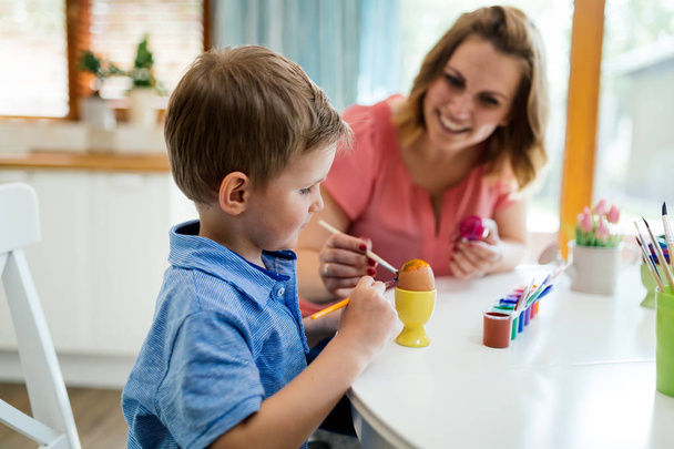 Happy young mother and son are sitting at a table painting Easter eggs - Foto, Bild