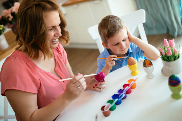 Happy young mother and son are sitting at a table painting Easter eggs - Foto, Imagen