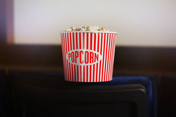 Balde com pipocas saborosas na cadeira de cinema
 - Foto, Imagem