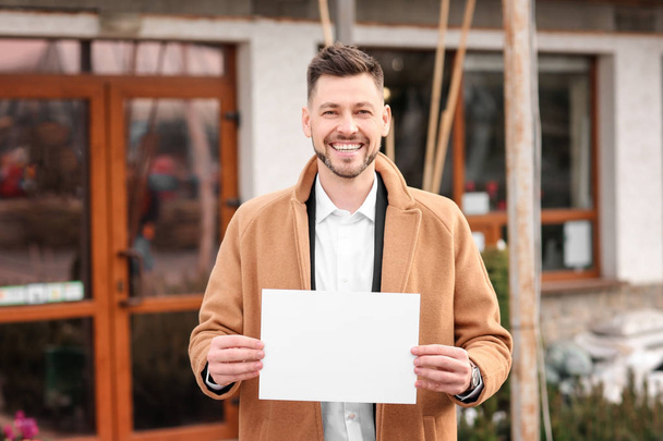 Business owner holding blank paper near his store, outdoors - Valokuva, kuva