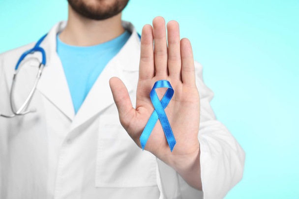 Doctor showing blue ribbon on color background. Cancer awareness concept - Φωτογραφία, εικόνα