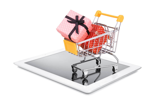 Tablet computer and small shopping cart with gift boxes on white background. Internet shopping concept - Zdjęcie, obraz