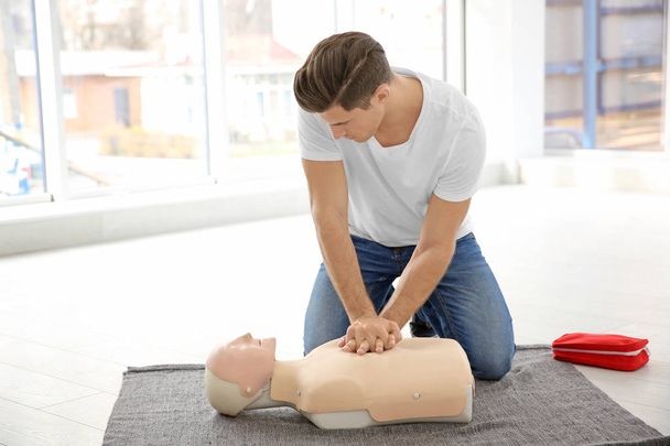 Young man practicing first aid on mannequin indoors - Фото, зображення