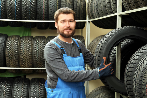 Male mechanic with car tire in automobile store - Fotoğraf, Görsel