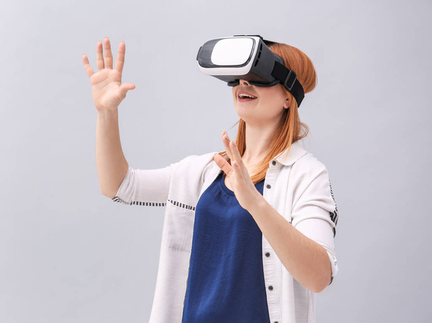 Woman with virtual reality headset on grey background - Photo, image